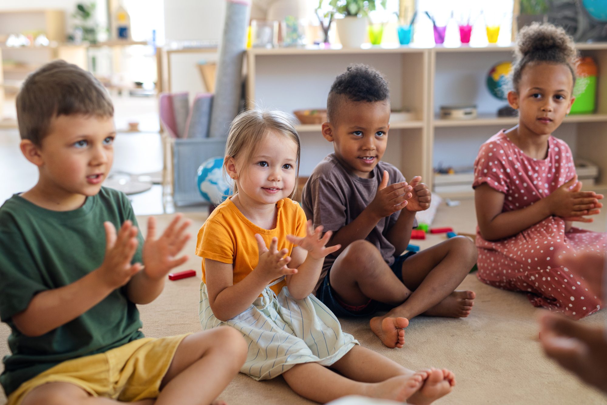 Preschoolers sitting in a circle on the classroom carpet, clapping together