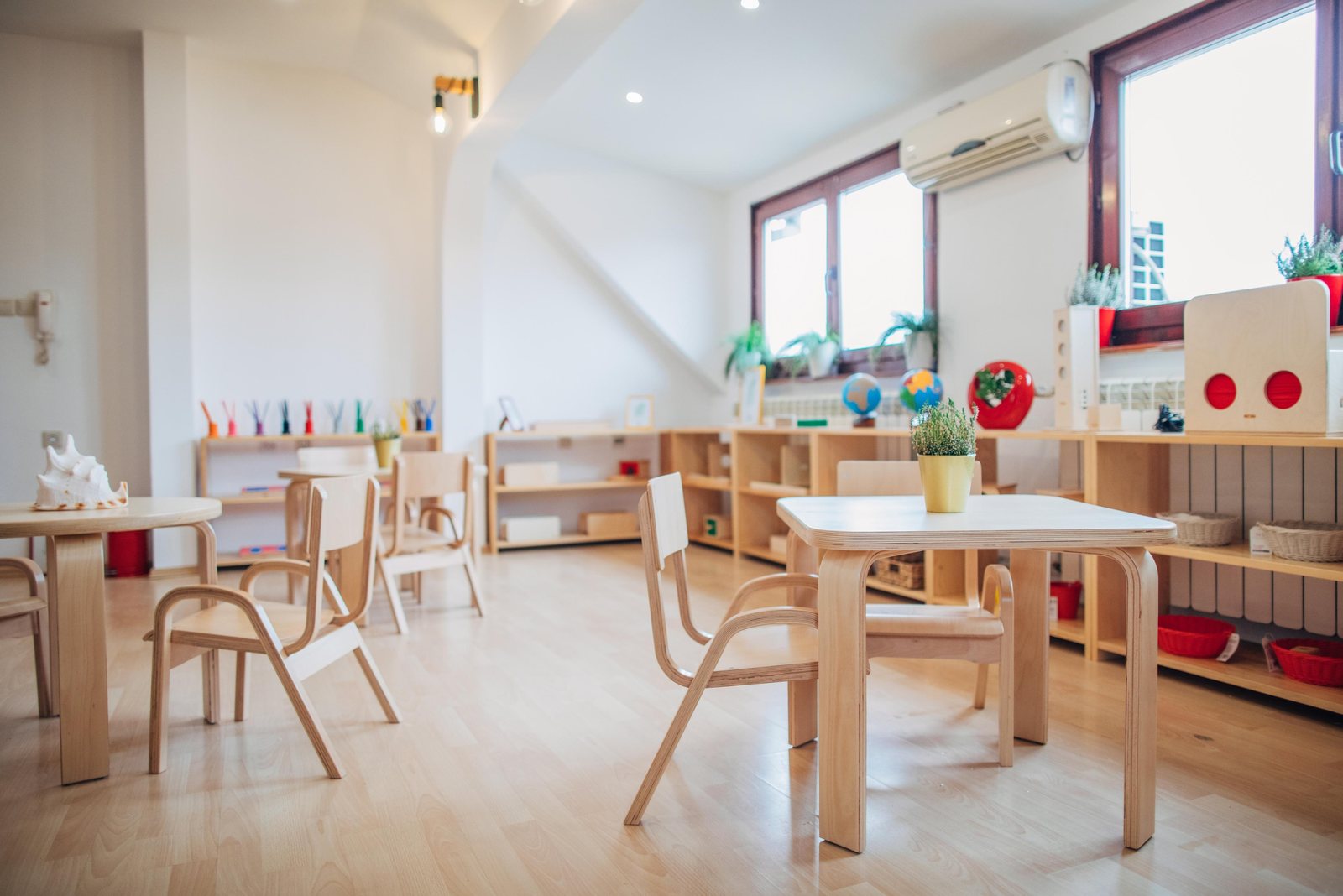 A bright Montessori classroom with child-sized wooden tables, chairs and low shelves of materials