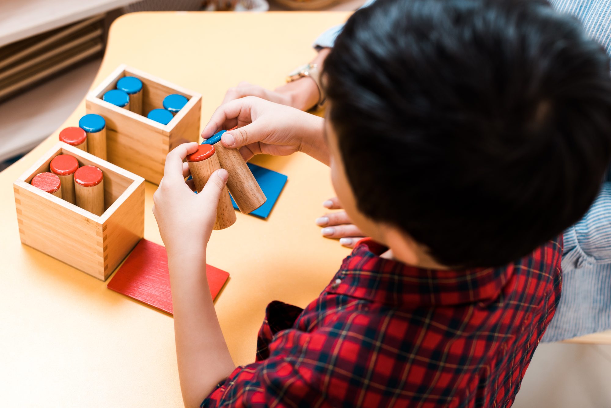 A child compares wooden Montessori sound cylinders at a table